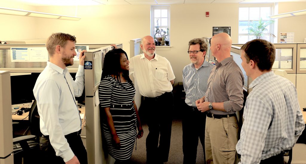 Six members of the Information Security Office talk in their workspace.