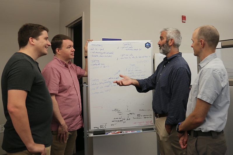 Four ITSers talk around a whiteboard