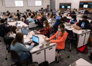 In the 111 Carroll Hall classroom, dozens of students sit at collaborative desks while using their laptops