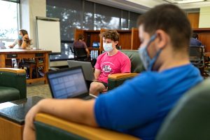 In the Undergraduate Library, students are using technology in comfy chairs, at a table, and in carrels