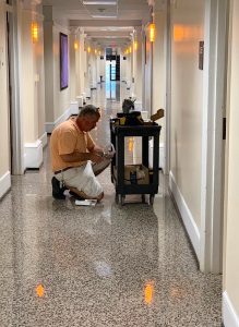 A man crouches by a utility cart in a hallway of Cobb dorm.