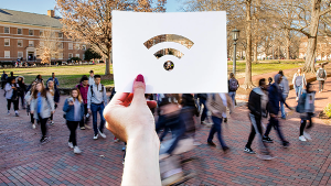 A woman's hand holds a piece of paper with the Wi-Fi symbol cut out. Behind her hand and showing through the Wi-Fi symbol is the quad at class change time.