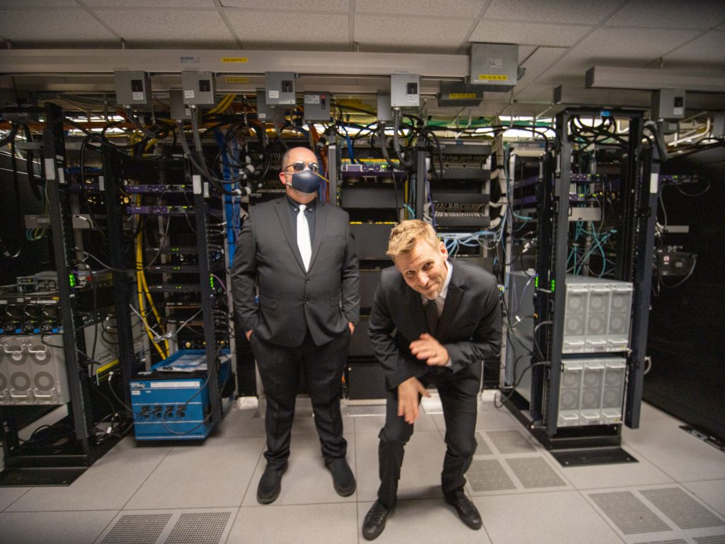 Michael Williams and Charlie Mewshaw pose in suits in front of computer equipment in the ITS data center.