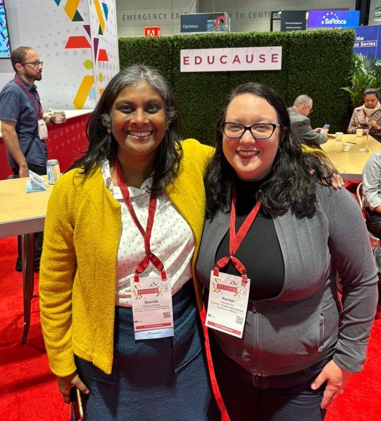 Brenda and her co-presenter Rachel smile broadly in front of an Educause sign