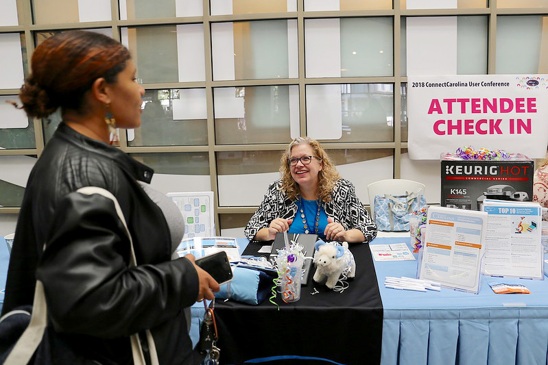 Sitting behind the check-in table at the user conference, Anita Collins greets an approaching woman 