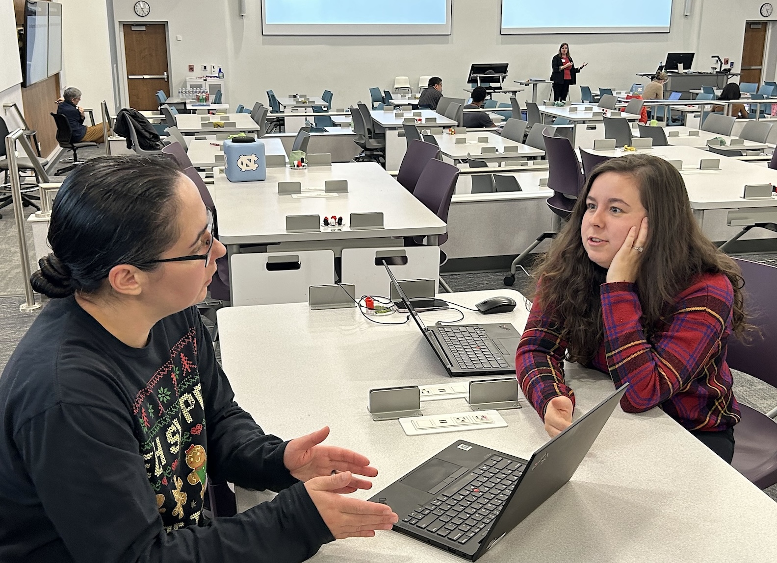 Two ITS Educational Technologies staffers talk while a Center for Faculty Excellence representative trains faculty members in the front of a classroom.