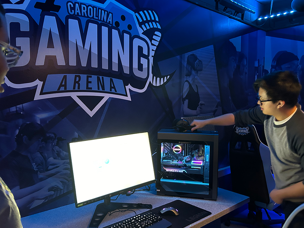 Alex Ho sets up a new Legion desktop on a desk directly underneath the Carolina Gaming Arena logo